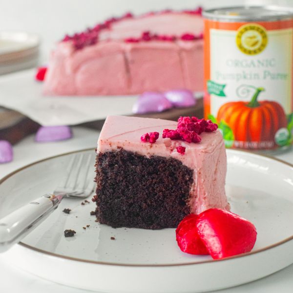A slice of eggless chocolate cake with raspberry frosting showing a can of Farmer's Market Foods Organic Pumpkin Puree